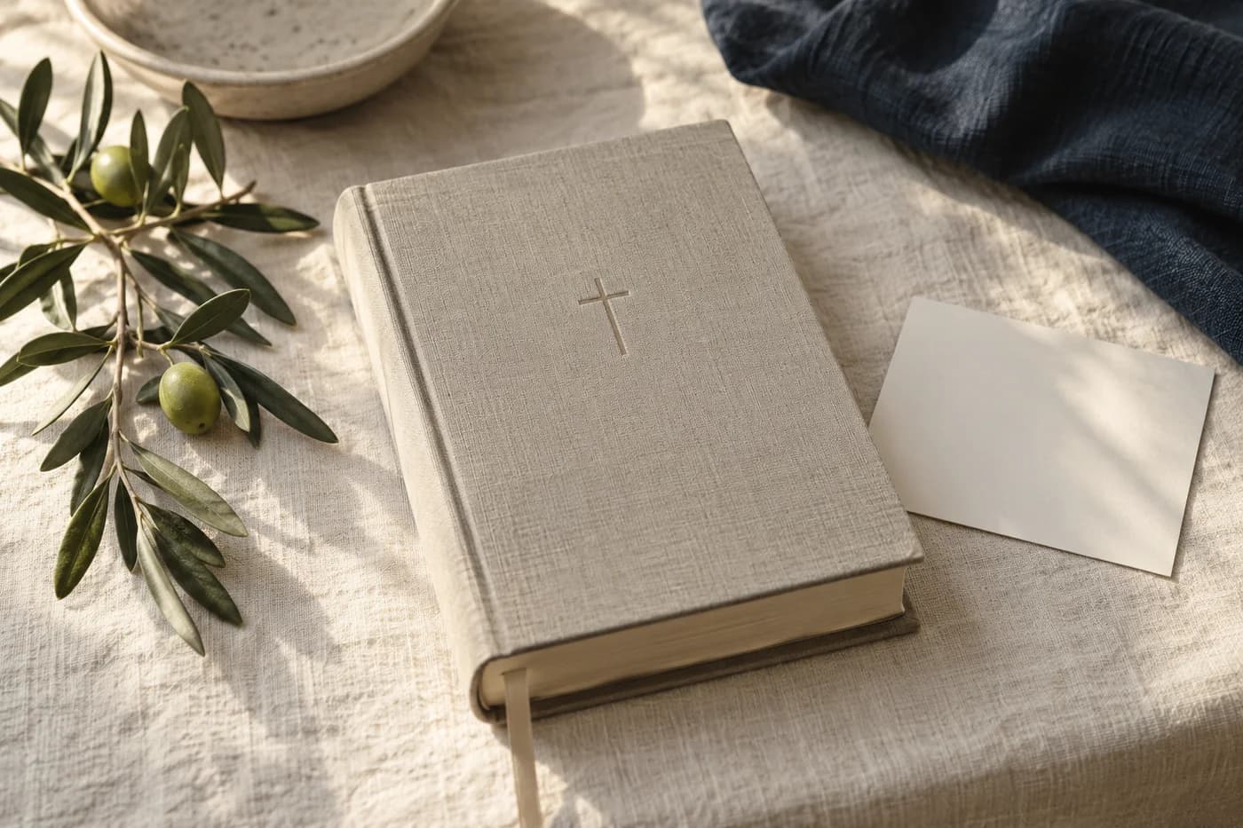 An illustrative linen-bound Bible beside an olive branch and dedication card